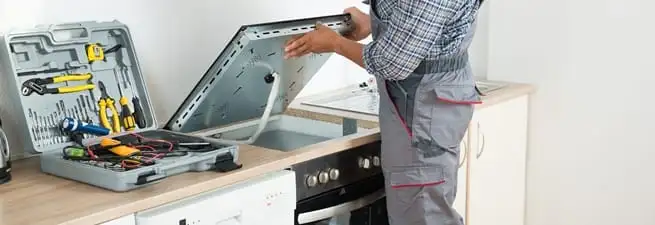 Cooktop repair technician lifting a built-in stovetop for service in Henderson, NV