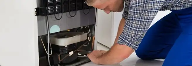 Refrigerator repair technician servicing the compressor and condenser area in Henderson, NV