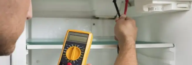 Refrigerator repair technician testing electrical components with a multimeter in Henderson, NV