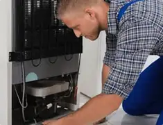 Refrigerator repair technician servicing the compressor and condenser area in Henderson, NV